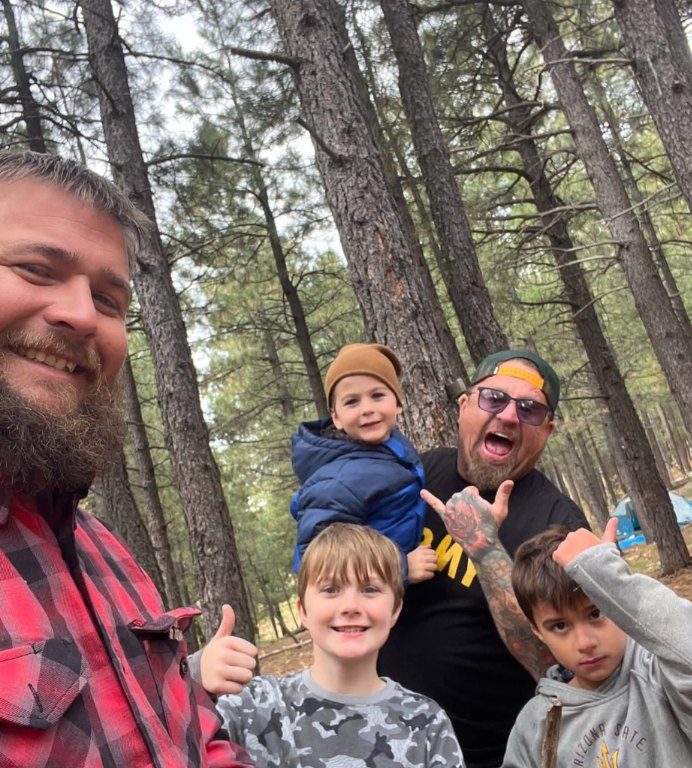 Two dads and three boys smiling among the ponderosa pines