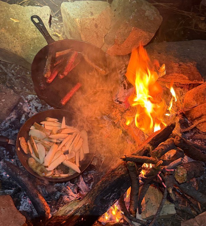 Hot dogs and potatoes cooking in skillets over the campfire