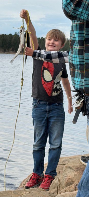A boy proudly holding up the trout he caught at the lake