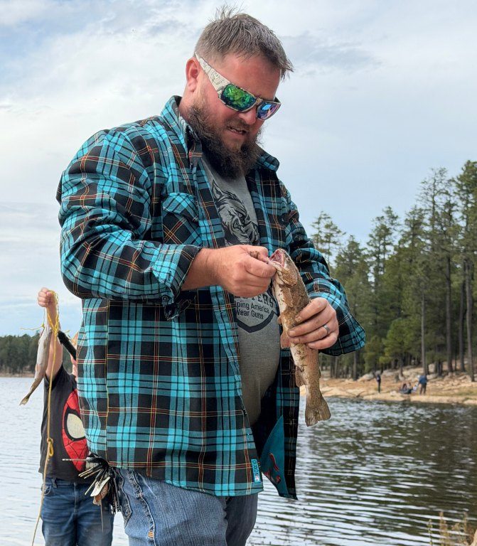 A dad taking a trout off the line at the lake