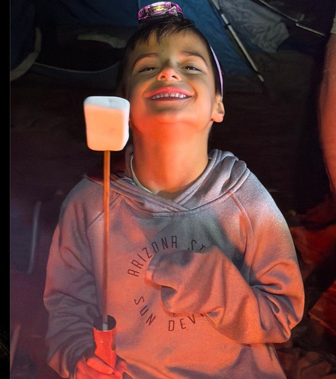 A boy grinning with a marshmallow on a roasting stick